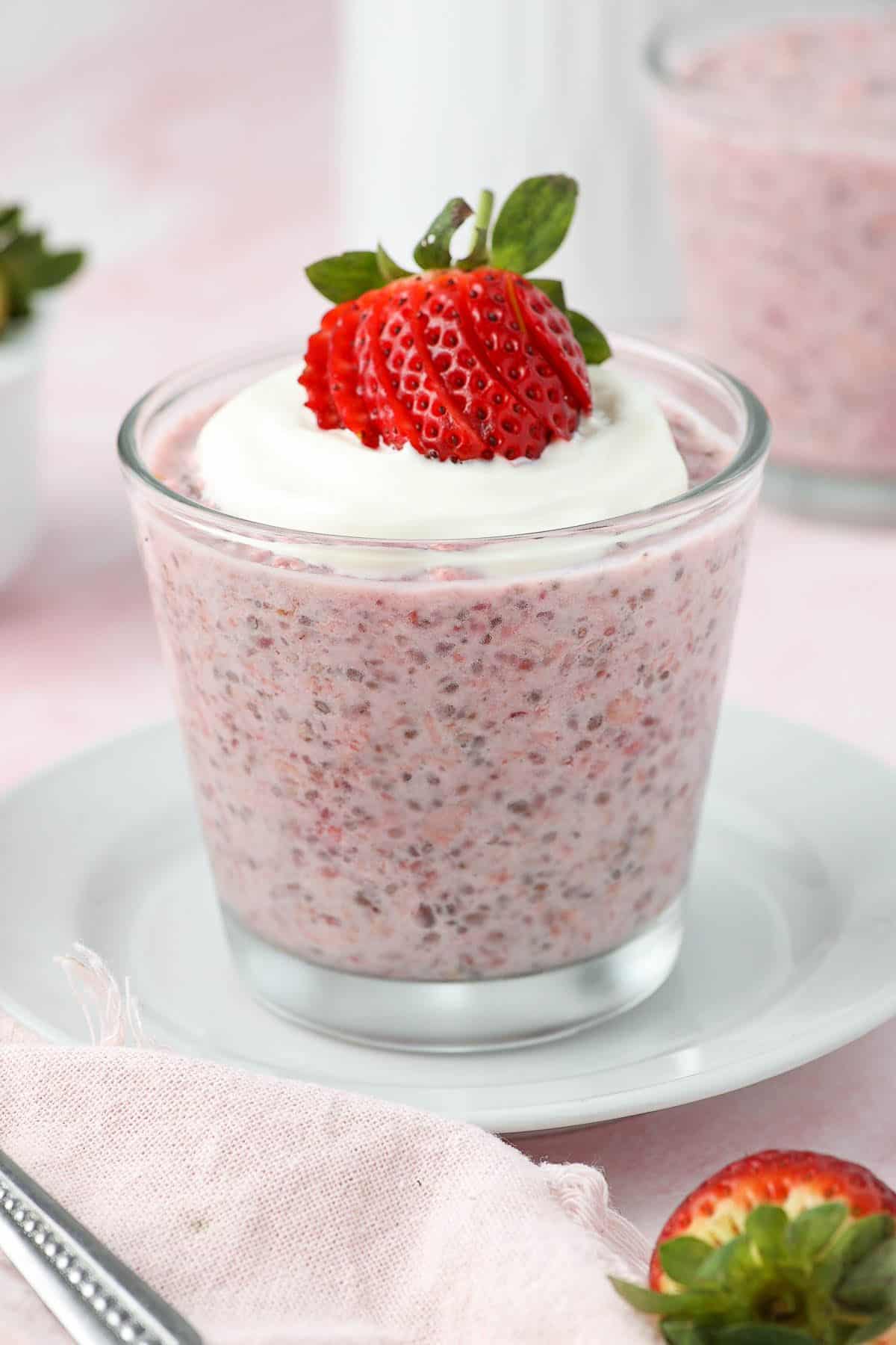 Glass jar of strawberry overnight oats, topped with yoghurt and a strawberry, sitting on a white saucer.