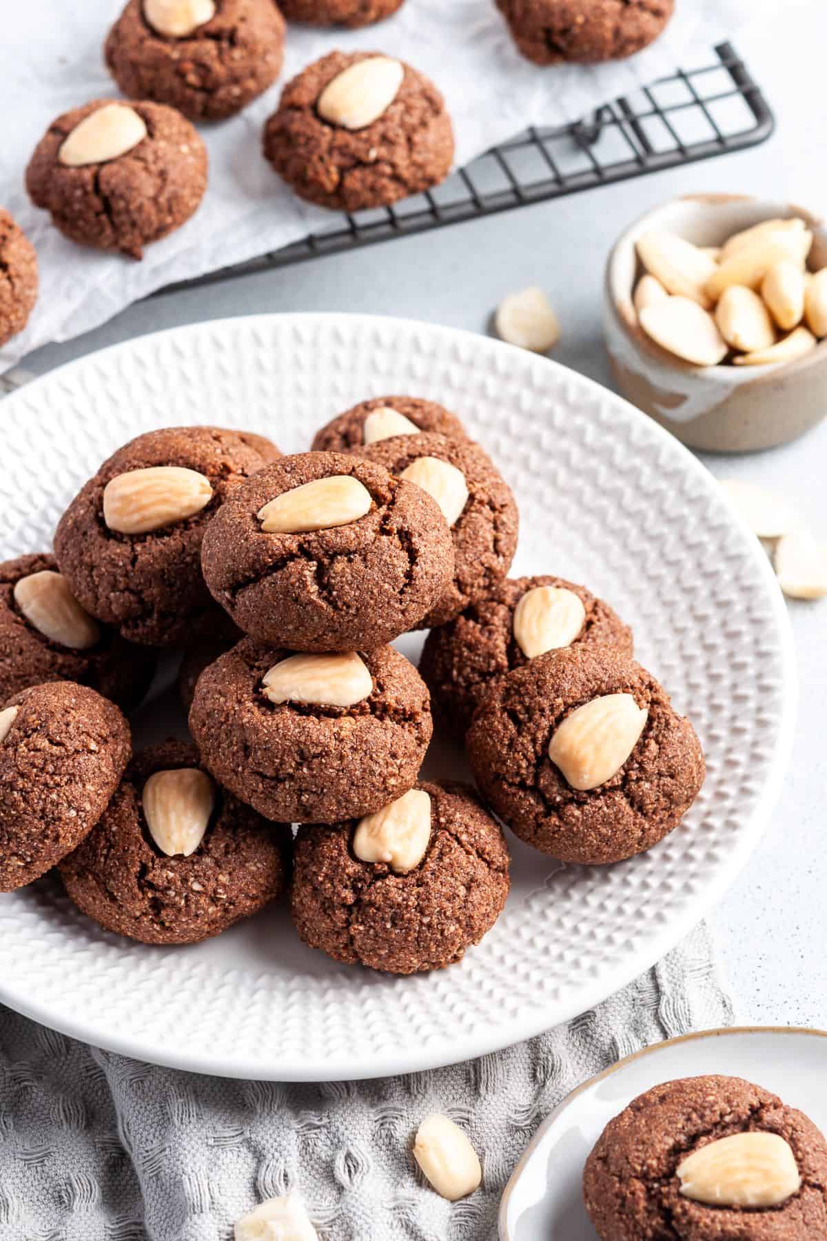 Round white plate with chocolate almond cookies, sitting on a grey cloth.
