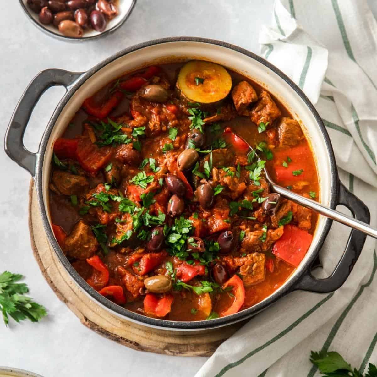 Dutch oven beef stew, with a silver serving spoon in dish which is garnished with parsley.