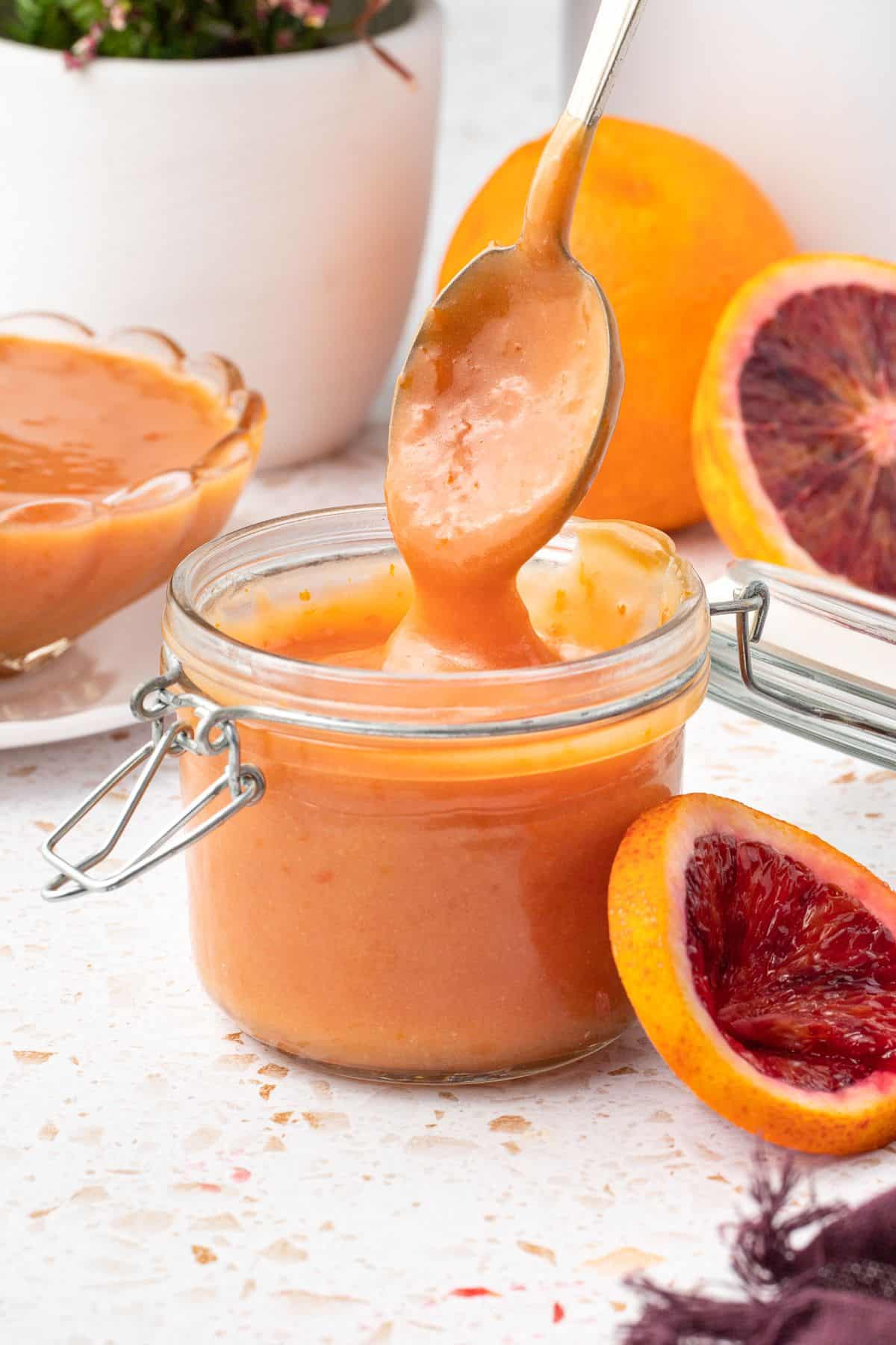 Glass jar of blood orange curd, with a spoon lifting some out.