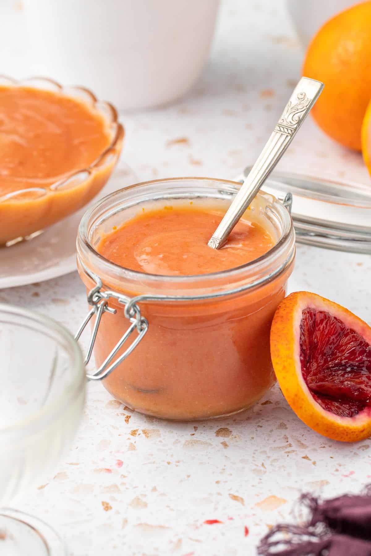 Glass jar of blood orange curd, with a spoon sitting in jar.