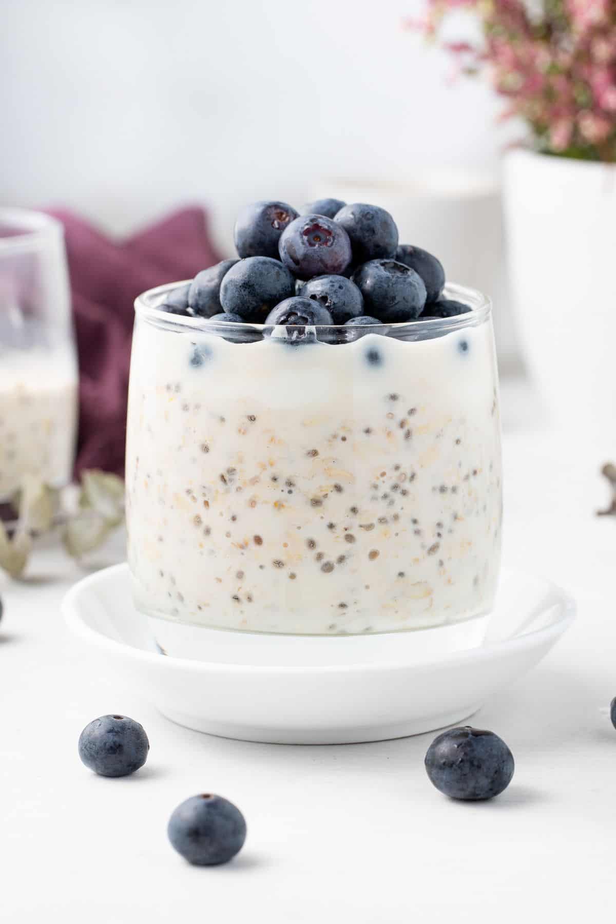 Glass jar of overnight oats topped with yoghurt and blueberries, sitting on a small round white plate.