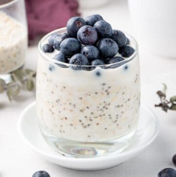 Glass jar of overnight oats topped with yoghurt and blueberries, sitting on a small round white plate.