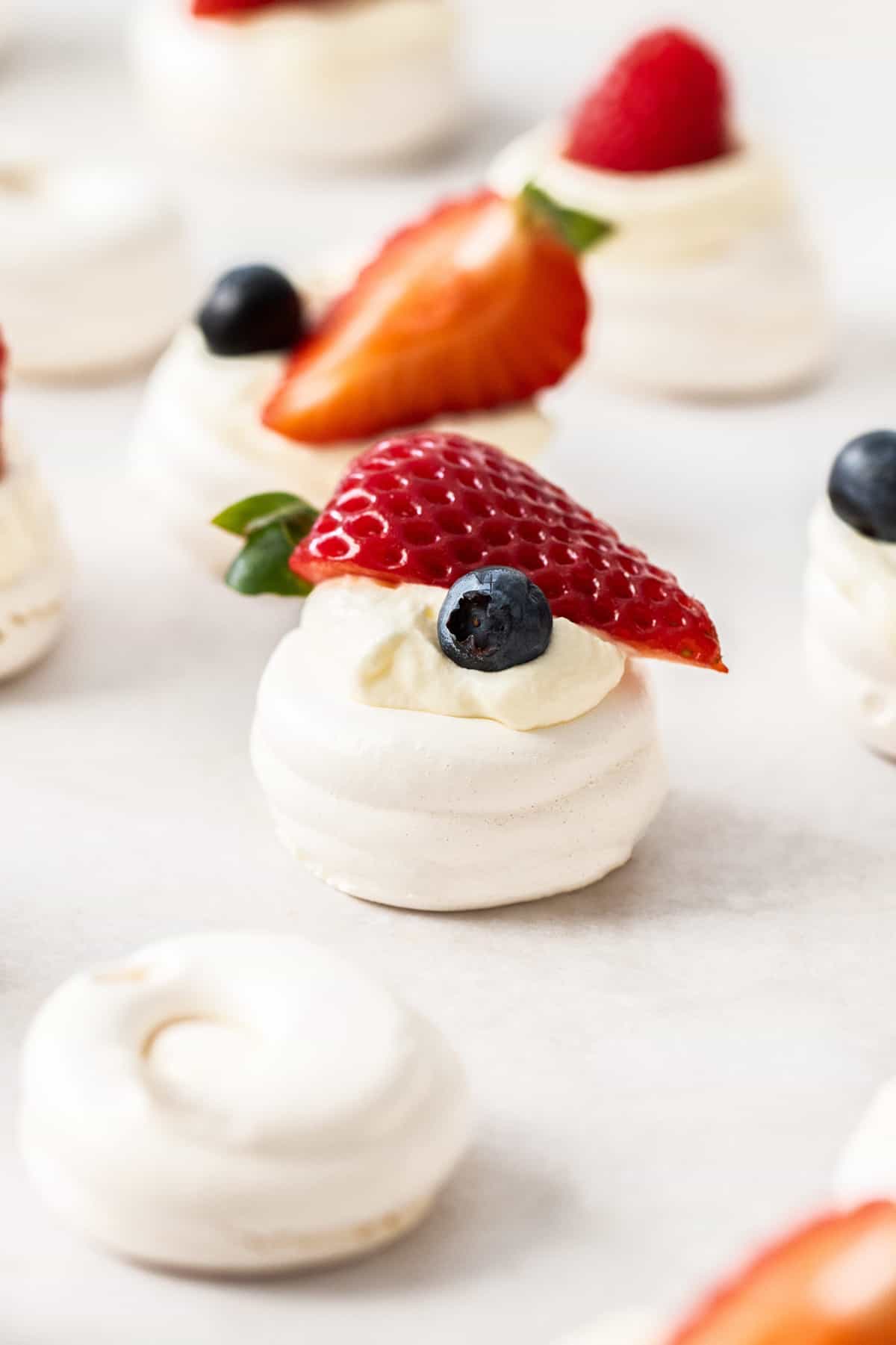 Mini meringue nests, with some cream and fresh berries, sitting on a tray.