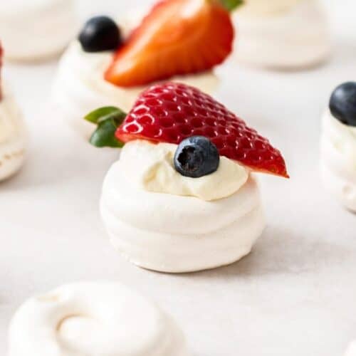 Mini meringue nests, with some cream and fresh berries, sitting on a tray.