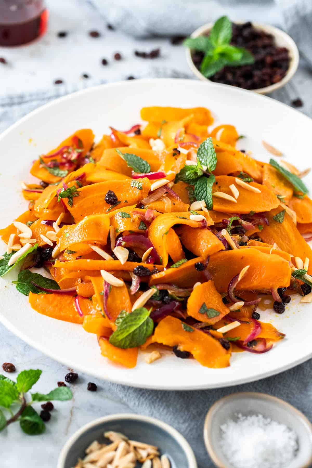 Round white dish of carrot salad, garnished with slivered almonds and mint leaves.