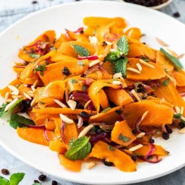 Round white dish of carrot salad, garnished with slivered almonds and mint leaves.