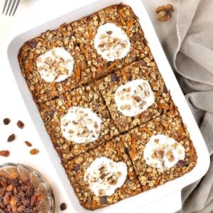 White rectangular dish of baked carrot oatmeal, cut into six pieces and topped with yoghurt and chopped walnuts.