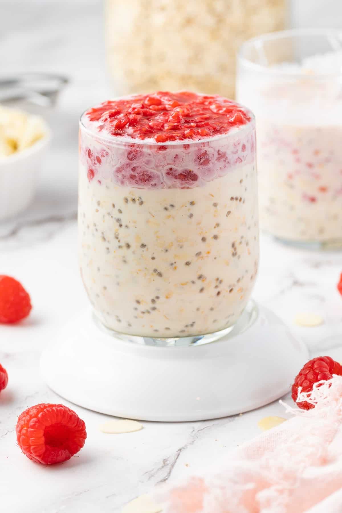 Glass jar of overnight oats topped with mashed raspberries, sitting on a white saucer.