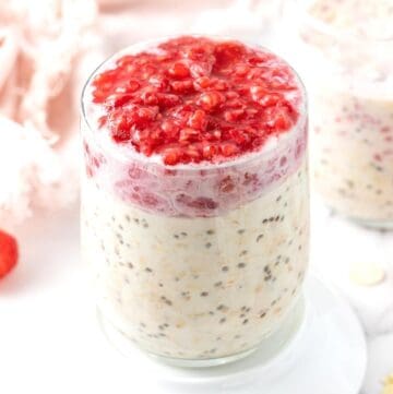 Glass jar of overnight oats topped with mashed raspberries, sitting on a white saucer.