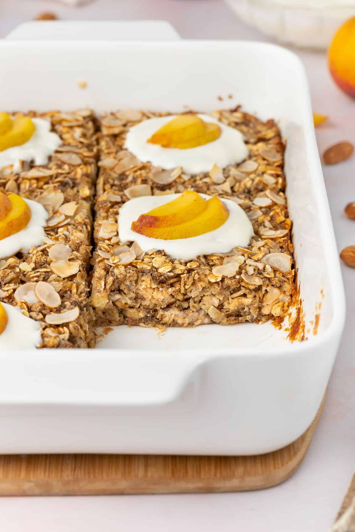 White rectangular dish with baked peach oatmeal, with one piece missing.