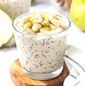 Glass of cinnamon overnight oats, topped with some chunks of fresh pear.