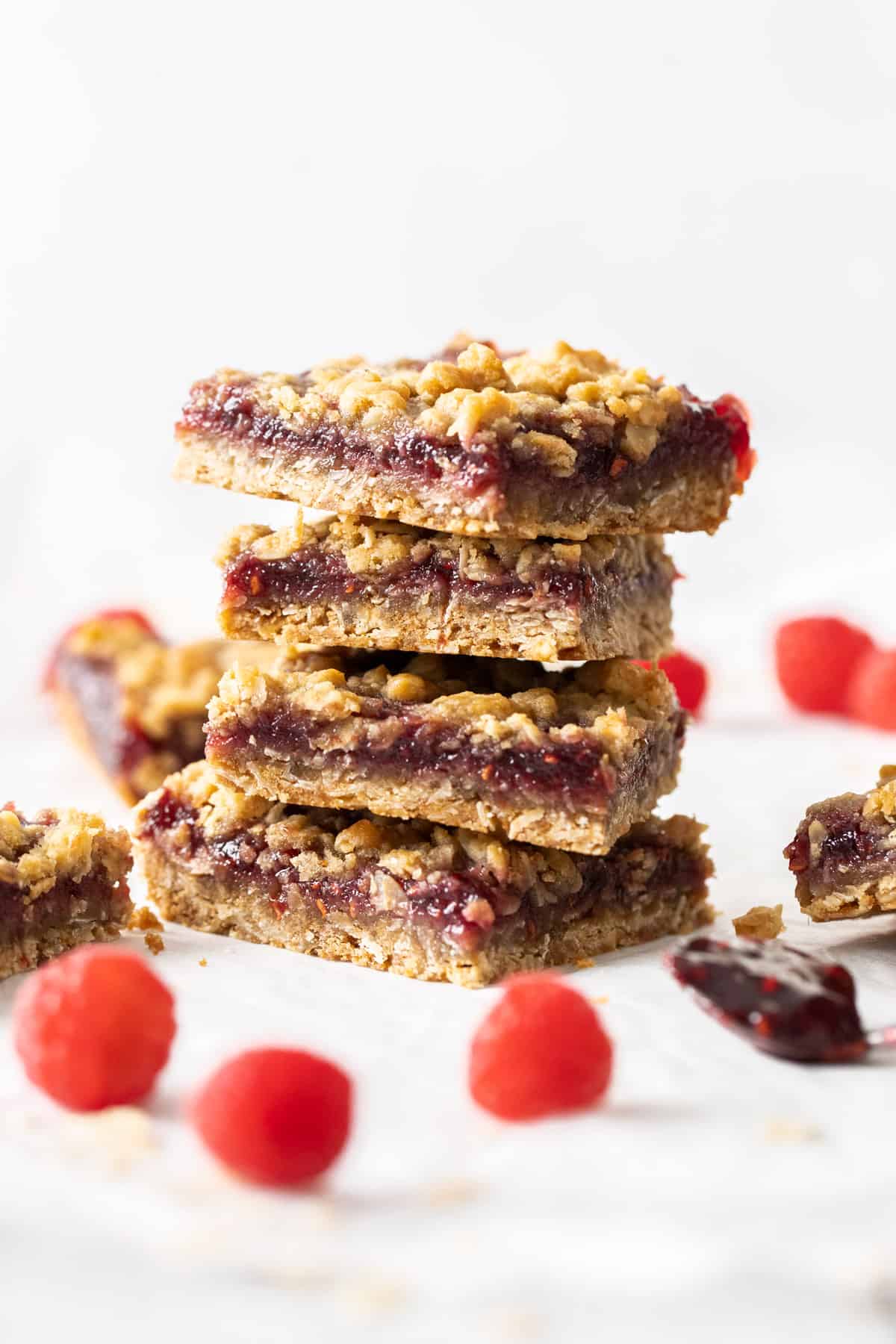 Stack of four jam bars, sitting on some parchment paper, with a few raspberries scattered around the edge.