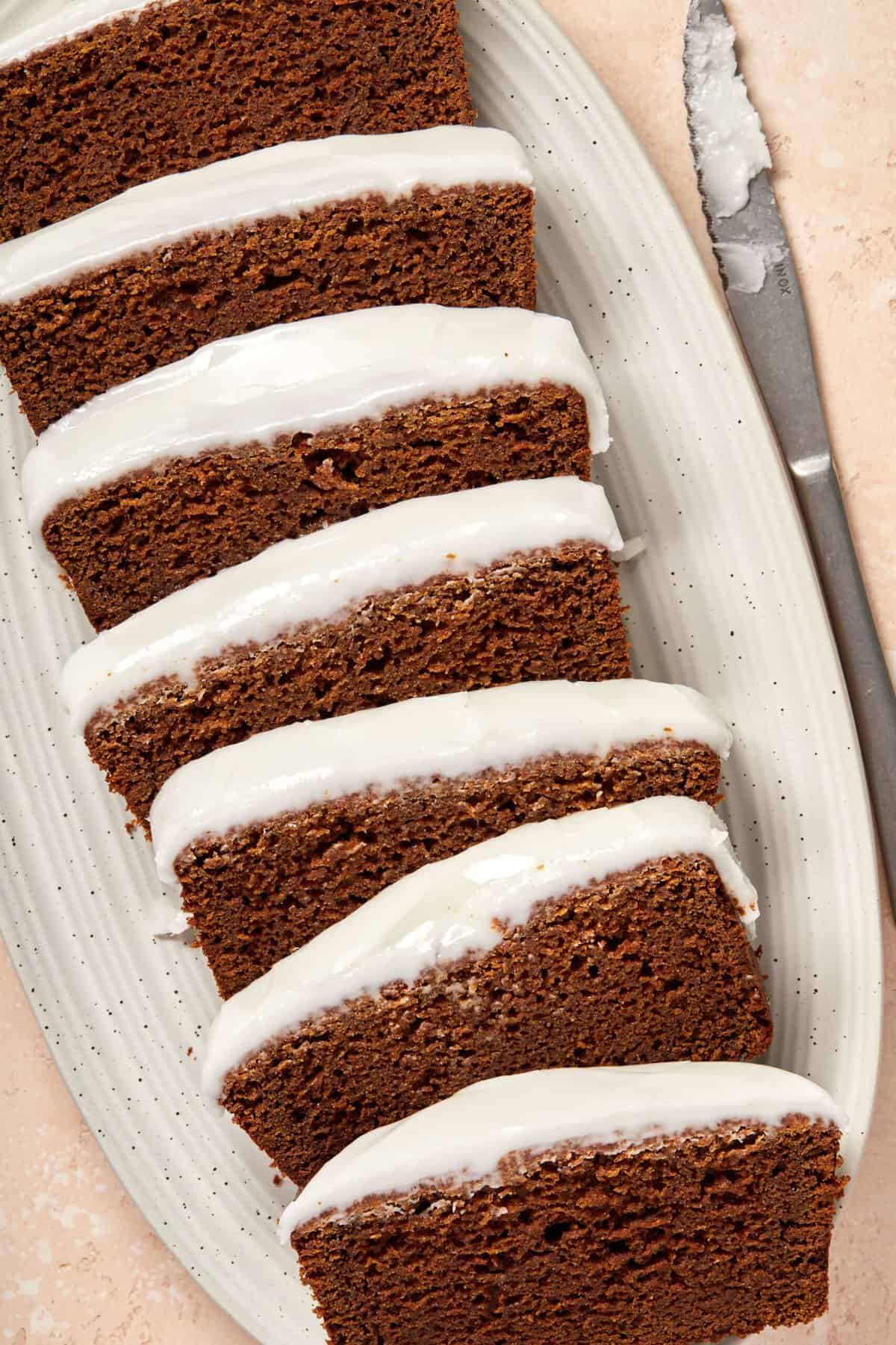 Slices of gingerbread loaf, sitting on a white oval dish with a knife on the side.