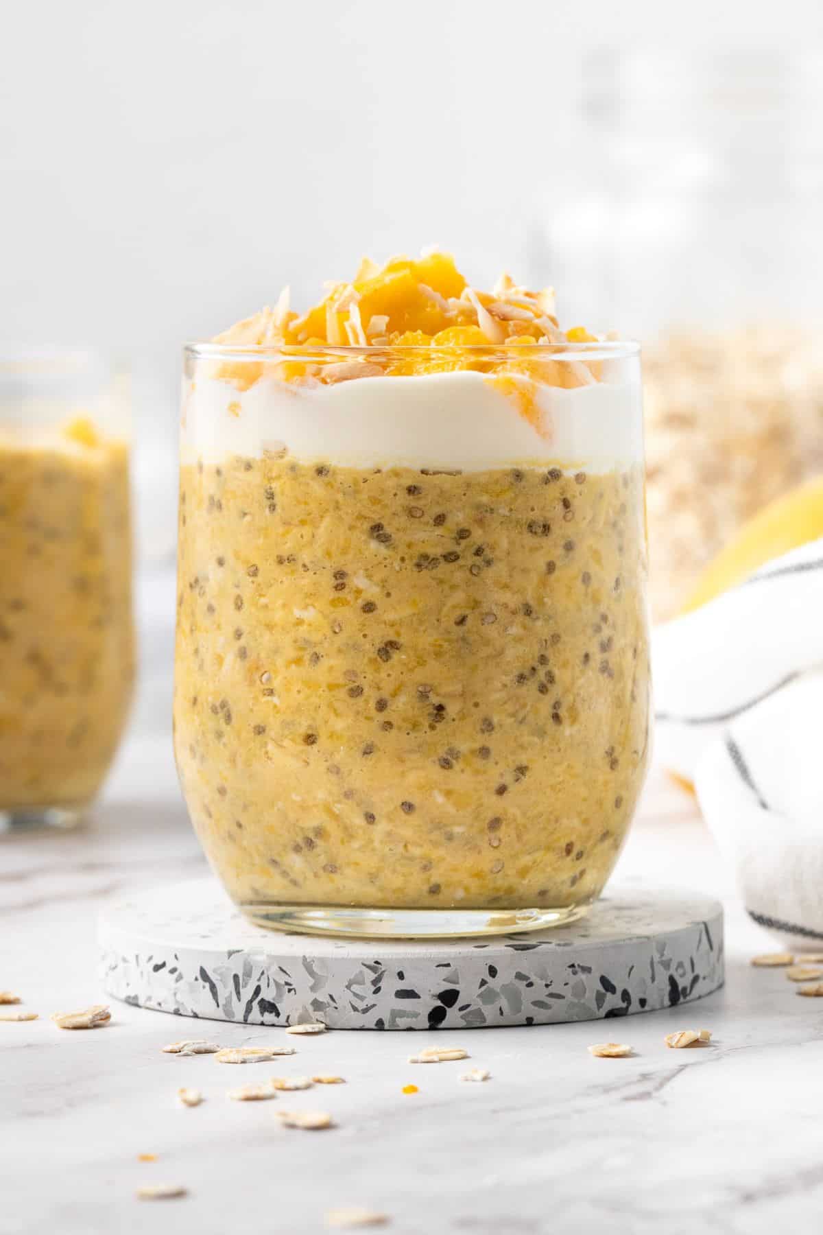 Glass jar of mango overnight oats, topping with yoghurt, mango pieces and some flaked coconut.