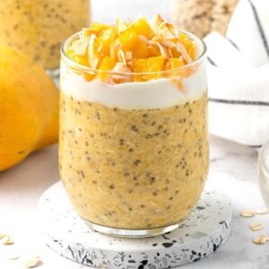 Glass jar of mango overnight oats, topping with yoghurt, mango pieces and some flaked coconut.