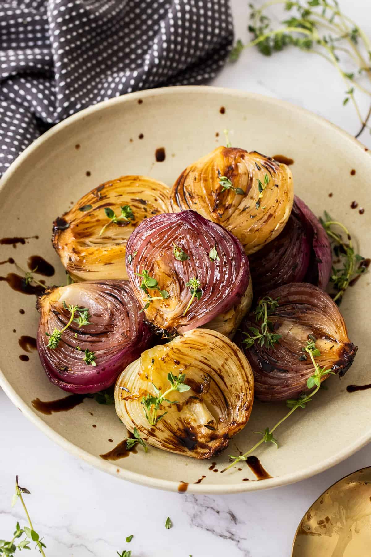 Round dish of roasted onions garnished with some fresh thyme leaves and drizzled with balsamic glaze.