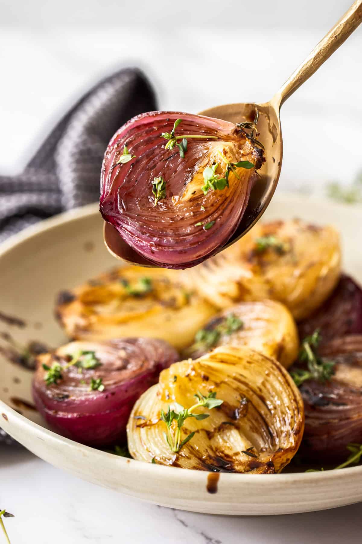 Spoon holding up a roasted onion half from a dish of roasted onions.
