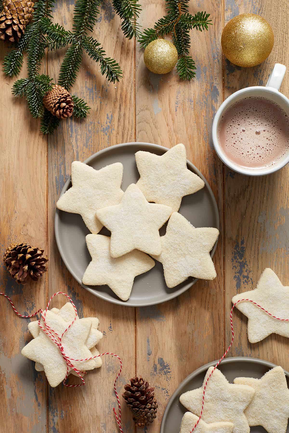 Round grey plate with five shortbread cookies, and some decorations, a cup of cocoa and cookies around the edge of the photo.