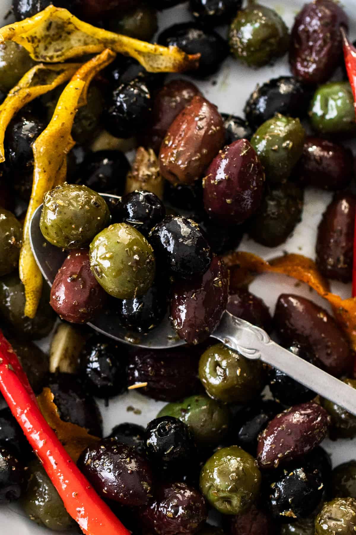 Up close shot of dish with roasted olives, and a silver spoon sitting in it.