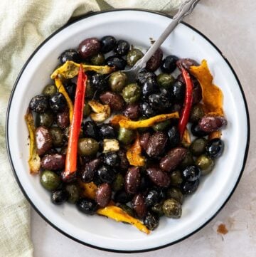 Round white dish with roasted olives, and a silver spoon sitting in it.