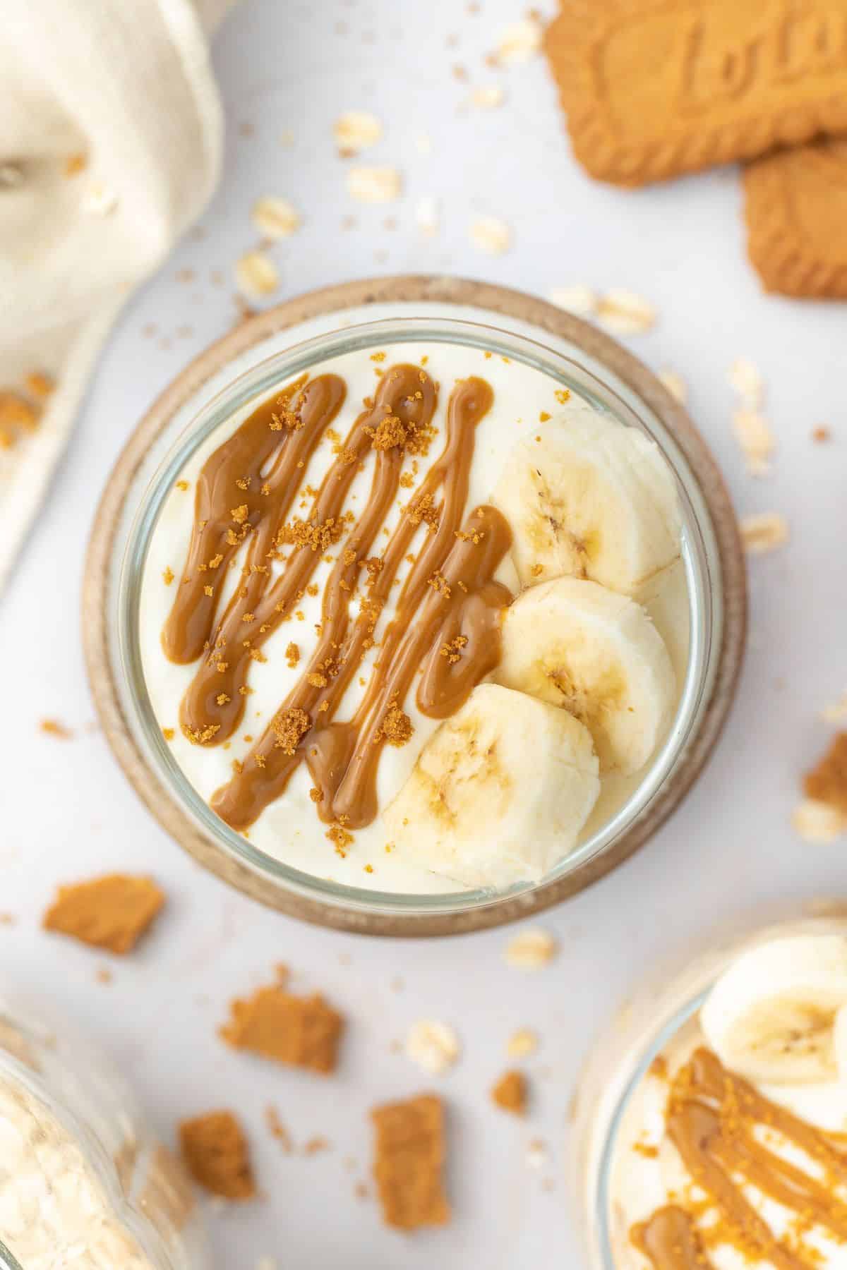 Overhead shot of overnight oats in a glass jar topped with yoghurt, slices of banana and a drizzle of Biscoff spread.