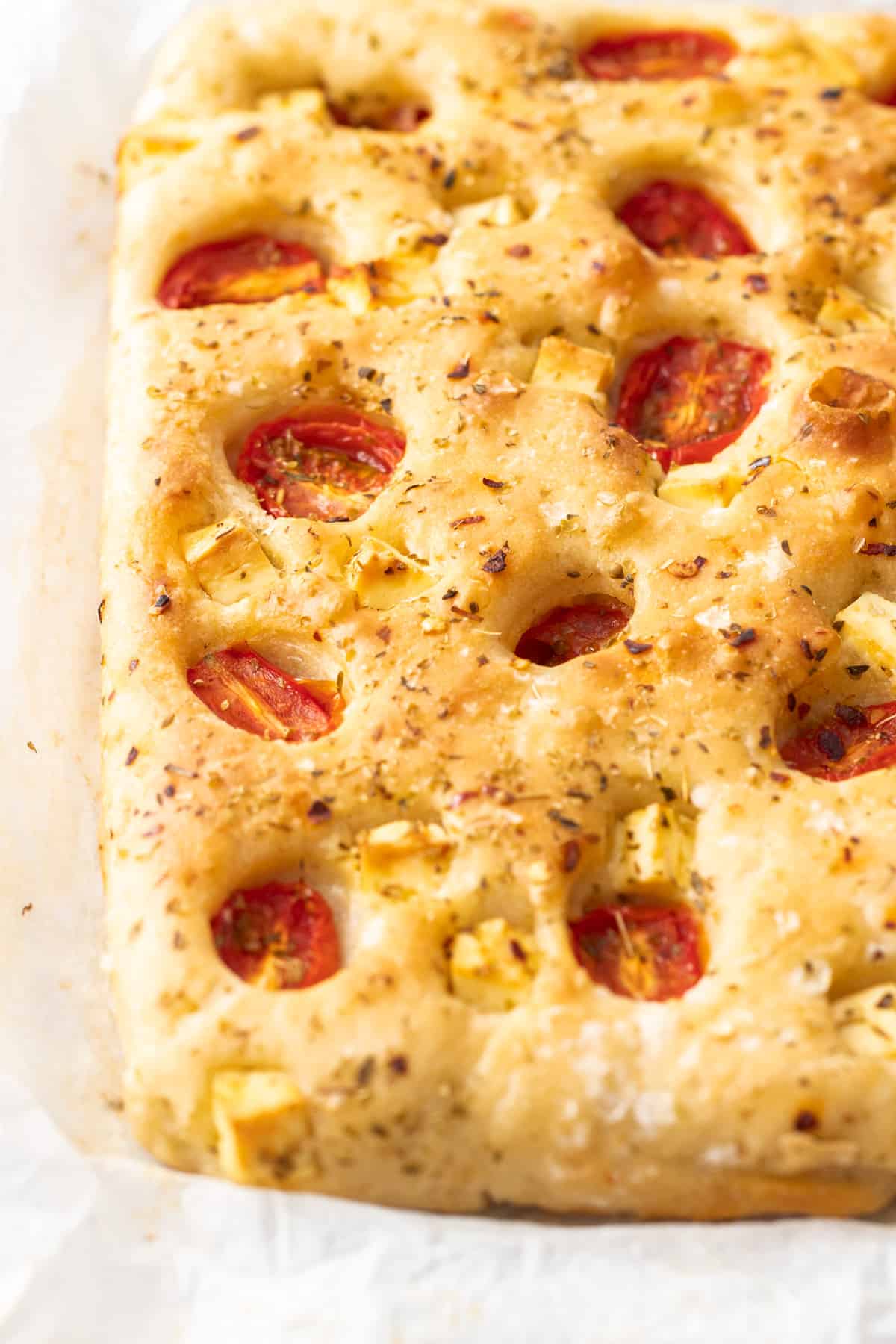 Up close shot of whole focaccia, studded with tomatoes and feta cheese.
