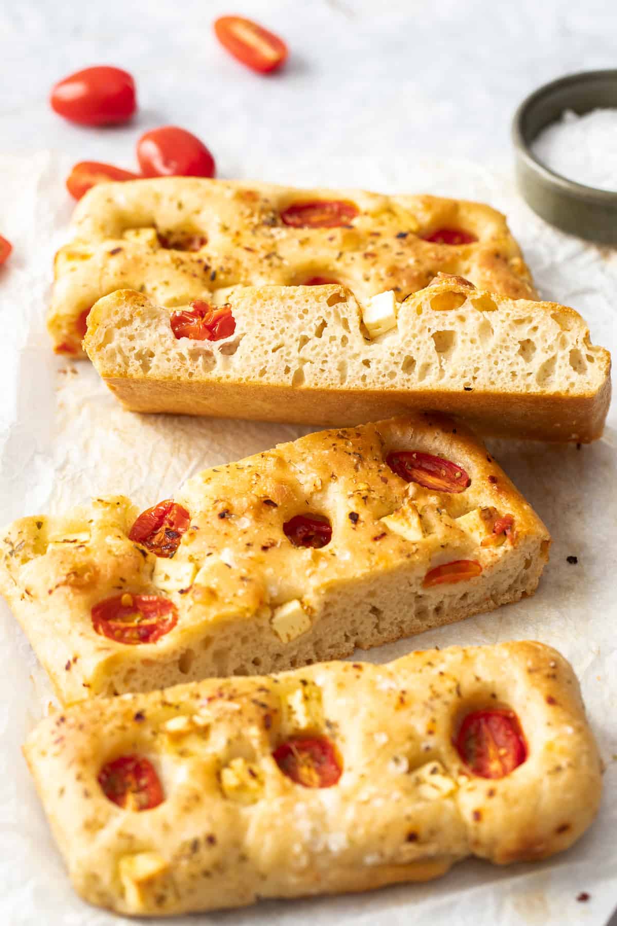 Four slices of focaccia, with one sitting on the edge to show the texture, sitting on some baking paper.