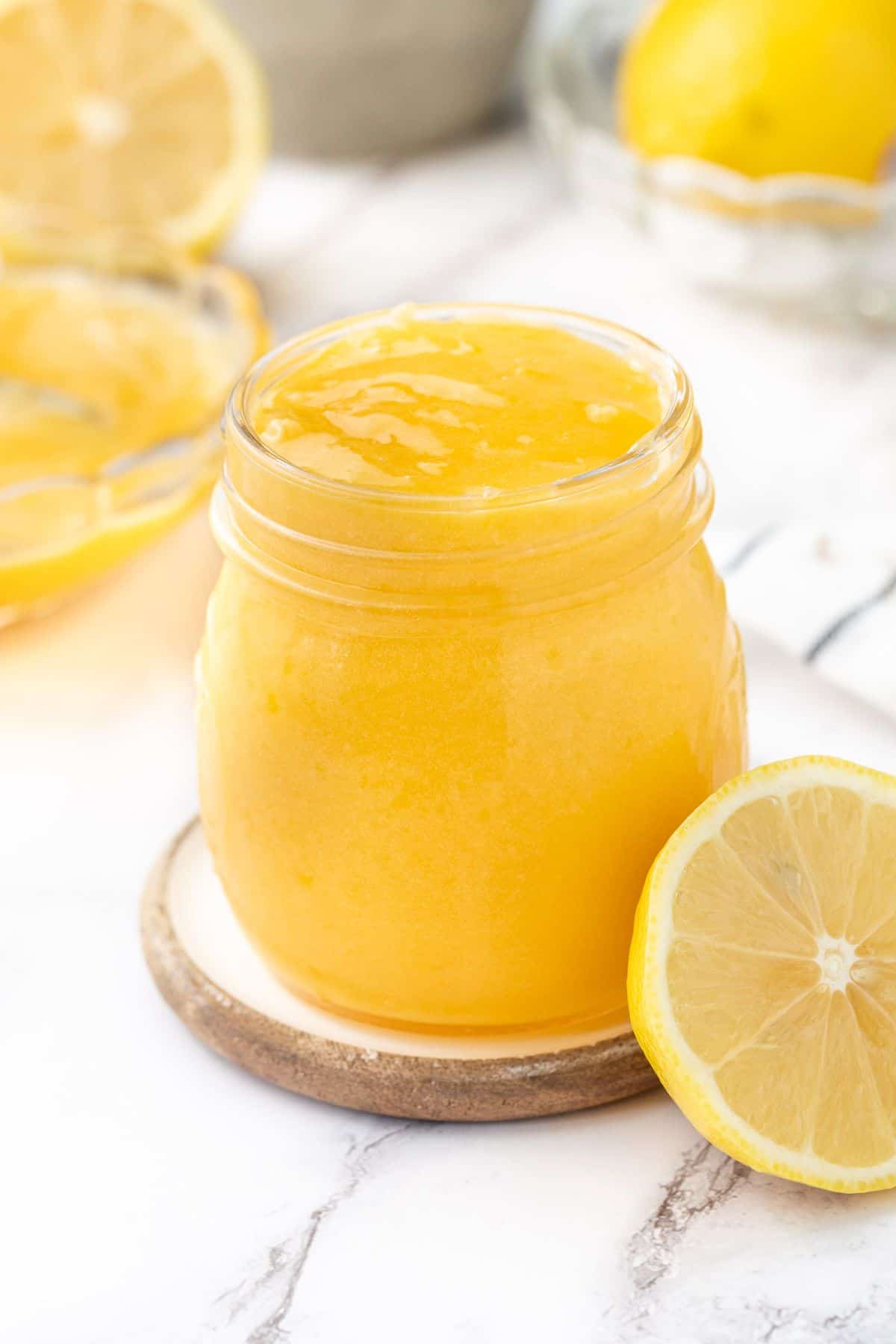 Glass jar of lemon curd, sitting on a small round saucer, with half a lemon on edge.