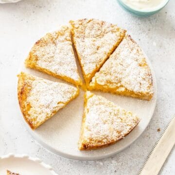 Overhead shot of Lemon Curd Cake, with a slice missing, sitting on a round white dish.