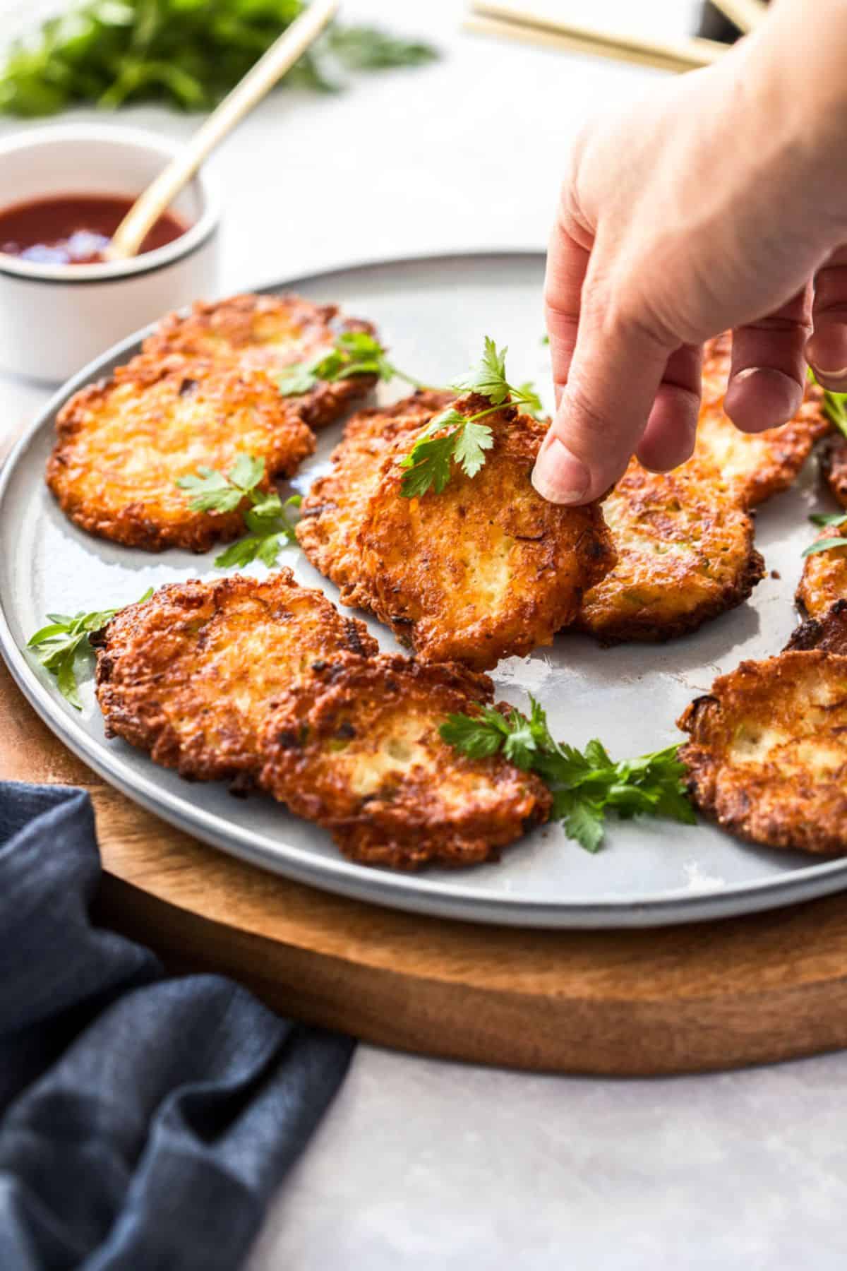 Hand reaching to pick up an onion fritter off a round grey plate.