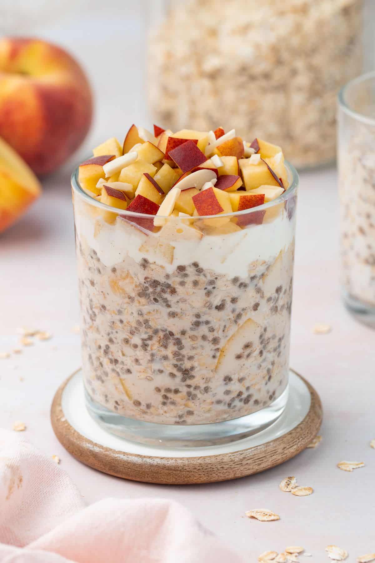Glass jar of overnight oats topped with yoghurt, cubes of fresh peach and flaked almonds.