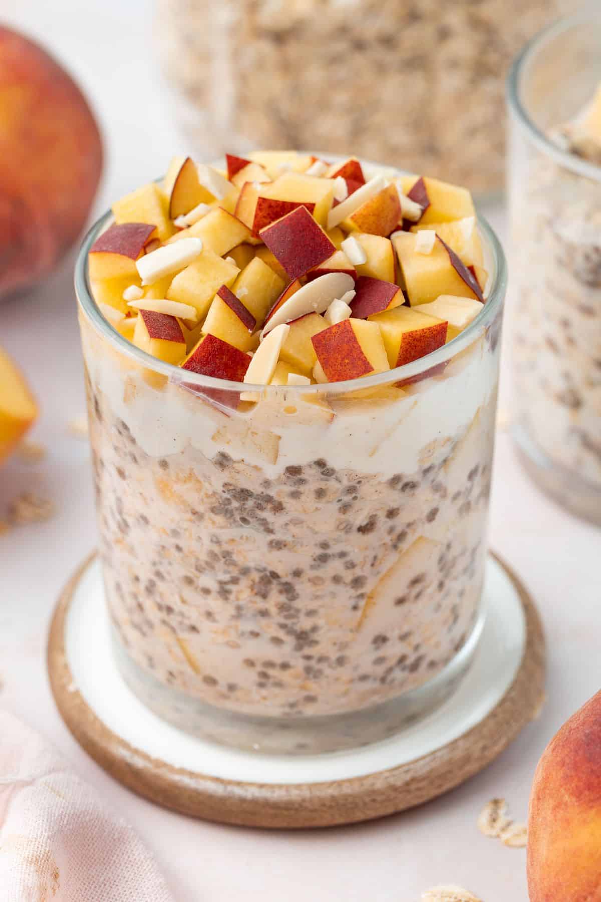 Glass jar of overnight oats topped with yoghurt, cubes of fresh peach and flaked almonds.