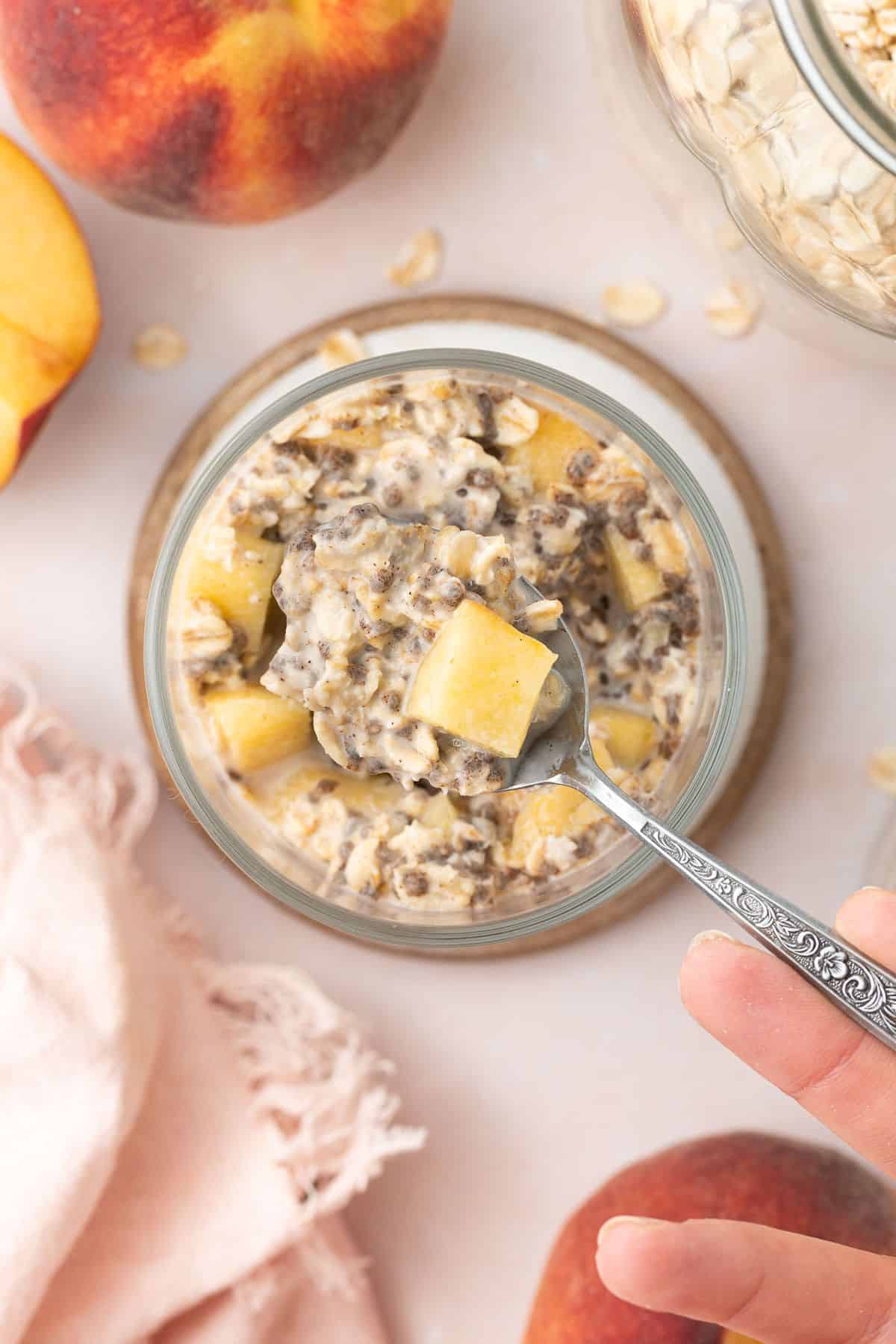 Spoon dipping into jar of peach overnight oats.