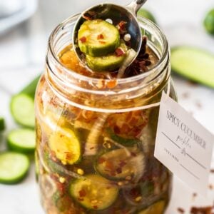 Jar of Spicy Cucumber Pickles, with a spoon reaching in to lift some pickles out of the jar.