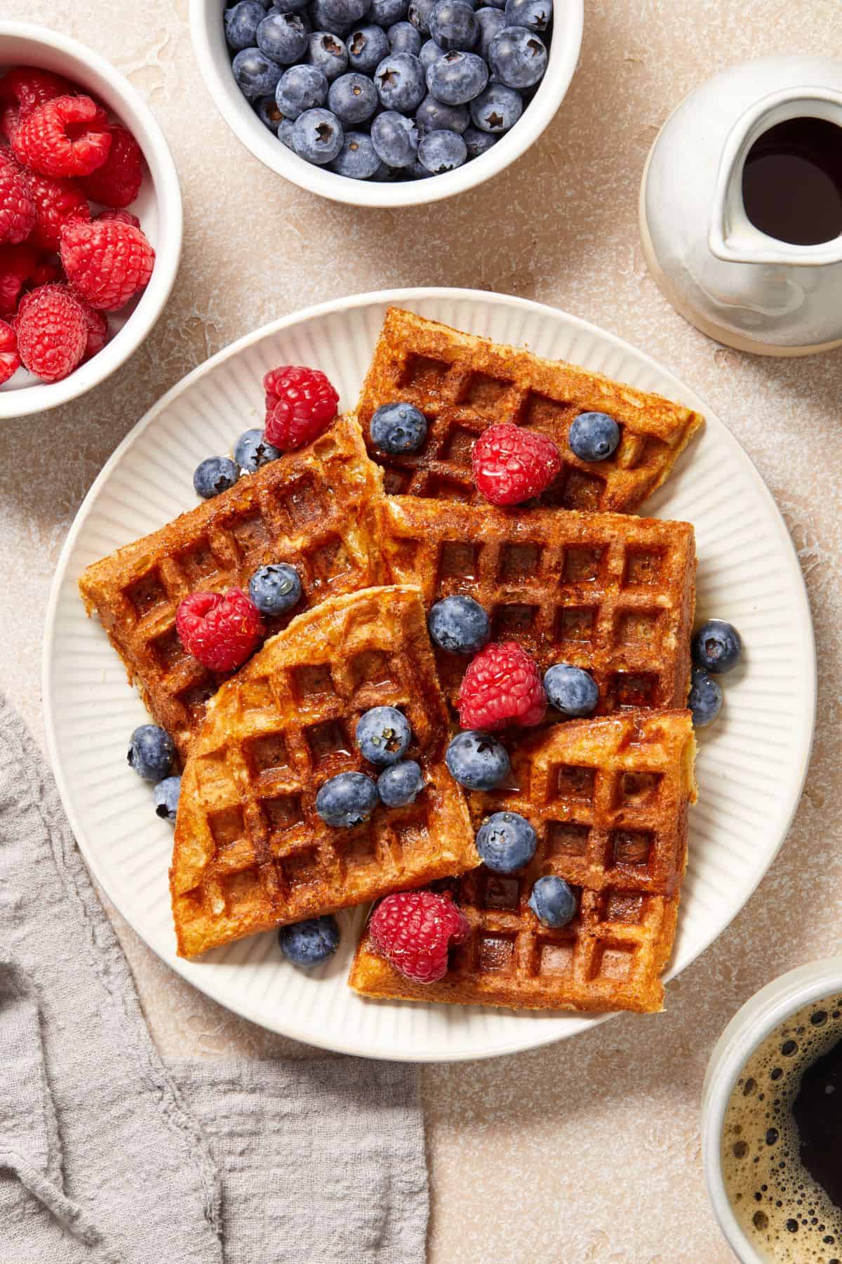 Round white plate with a serve of oat flour waffles, garnished with some raspberries and blueberries.