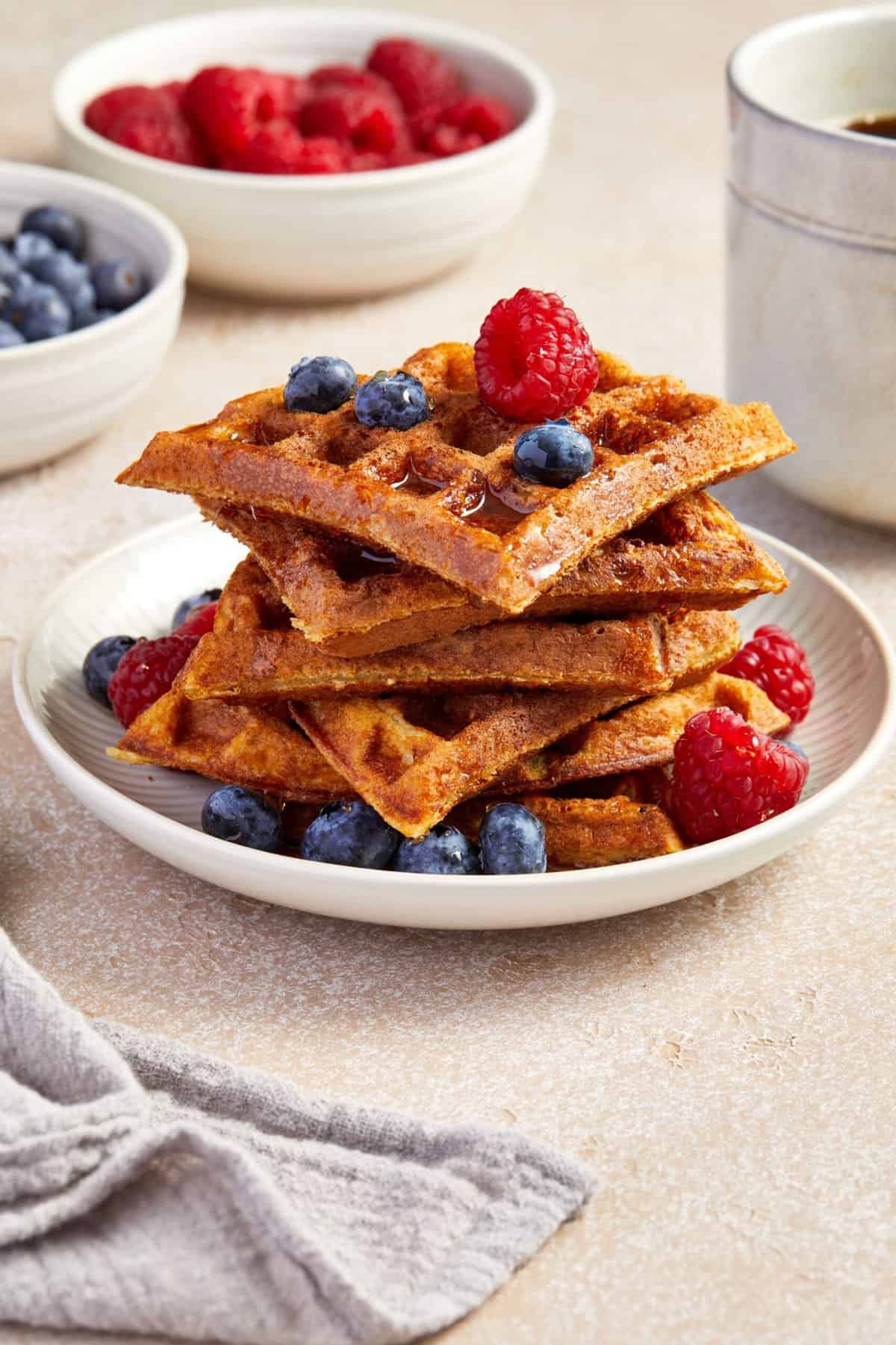 Round white plate with a stack of oat flour waffles, garnished with some raspberries and blueberries.