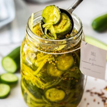 Jar of Cucumber Dill Pickles, with a spoon reaching in to lift some pickles out of the jar.