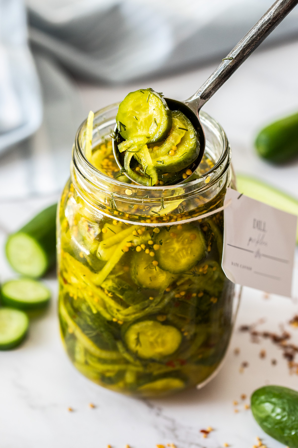 Jar of Cucumber Dill Pickles, with a spoon reaching in to lift some pickles out of the jar.