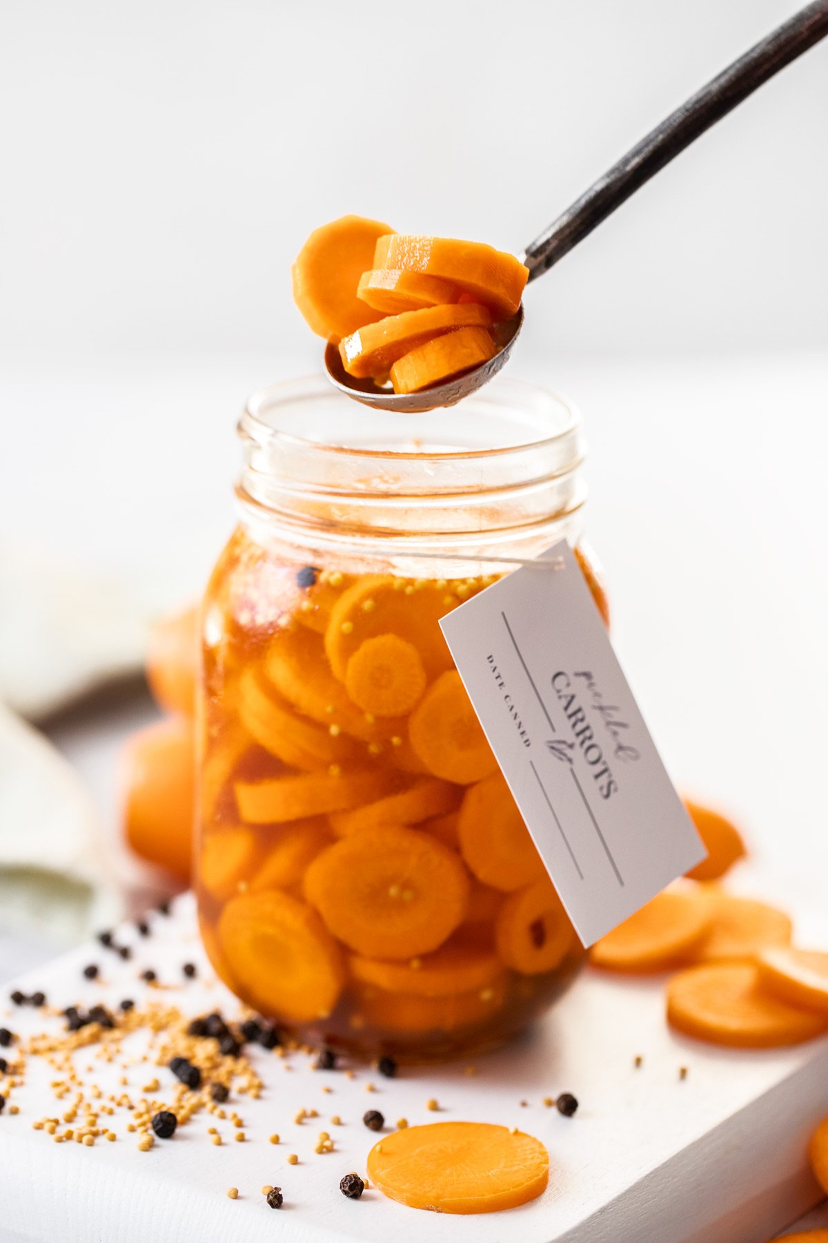 Jar of Pickled Carrots, with a spoon reaching in to lift some pickles out of the jar.