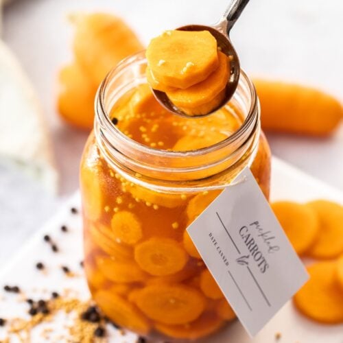 Jar of Pickled Carrots, with a spoon reaching in to lift some pickles out of the jar.