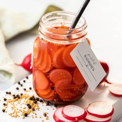 Glass jar of Pickled Radishes, with a label around the neck of the jar, and a spoon in the jar.