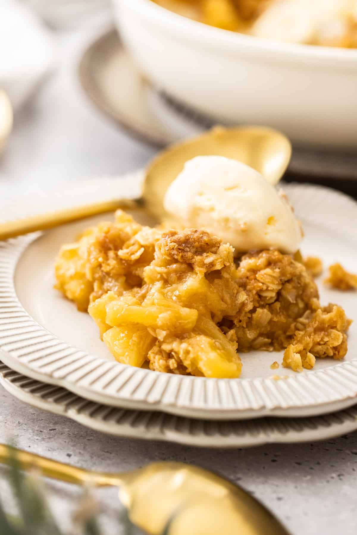 Serve of Pineapple Crisp, on a round white plate, with a scoop of ice cream and spoon on the side.