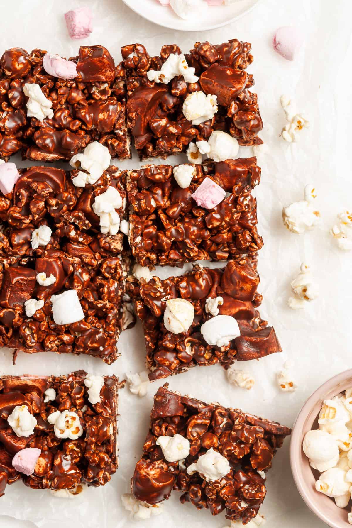 Eight cut squares of chocolate popcorn bars on some baking paper, with some popcorn scattered around the edges.