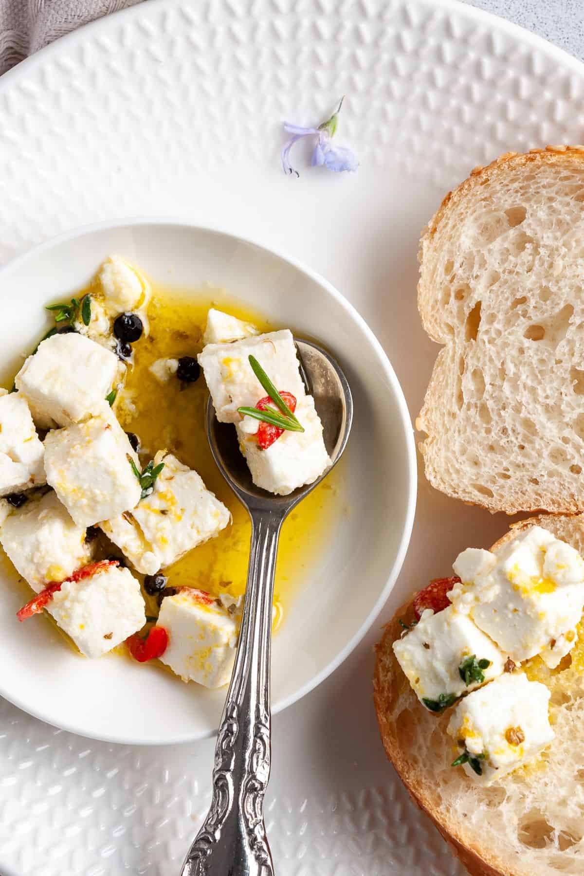 Small white plate with serving of feta, with a silver spoon scooping a piece of feta.