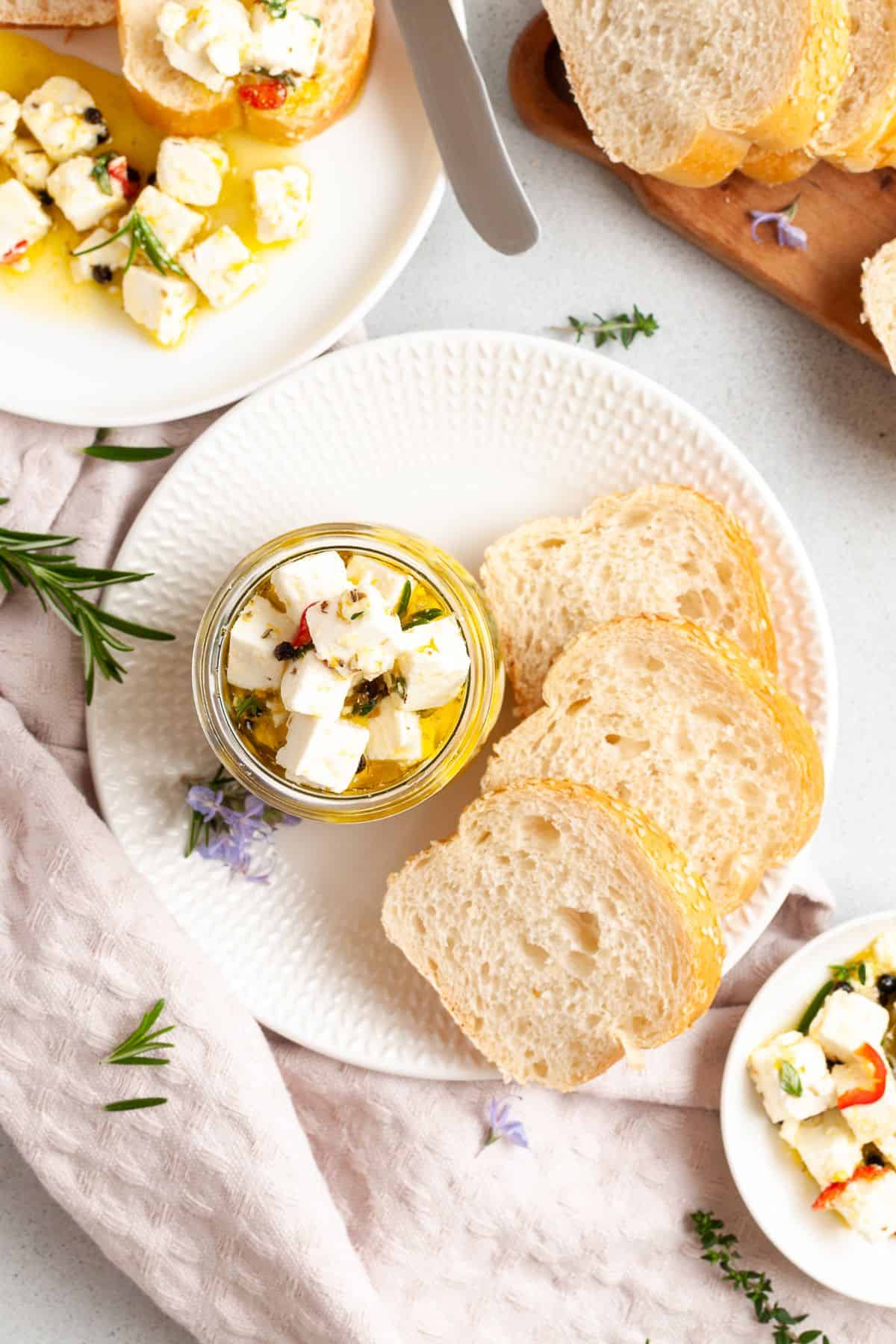 Two white plates with some feta cheese on the plate and some in a jar, and some slices of bread.