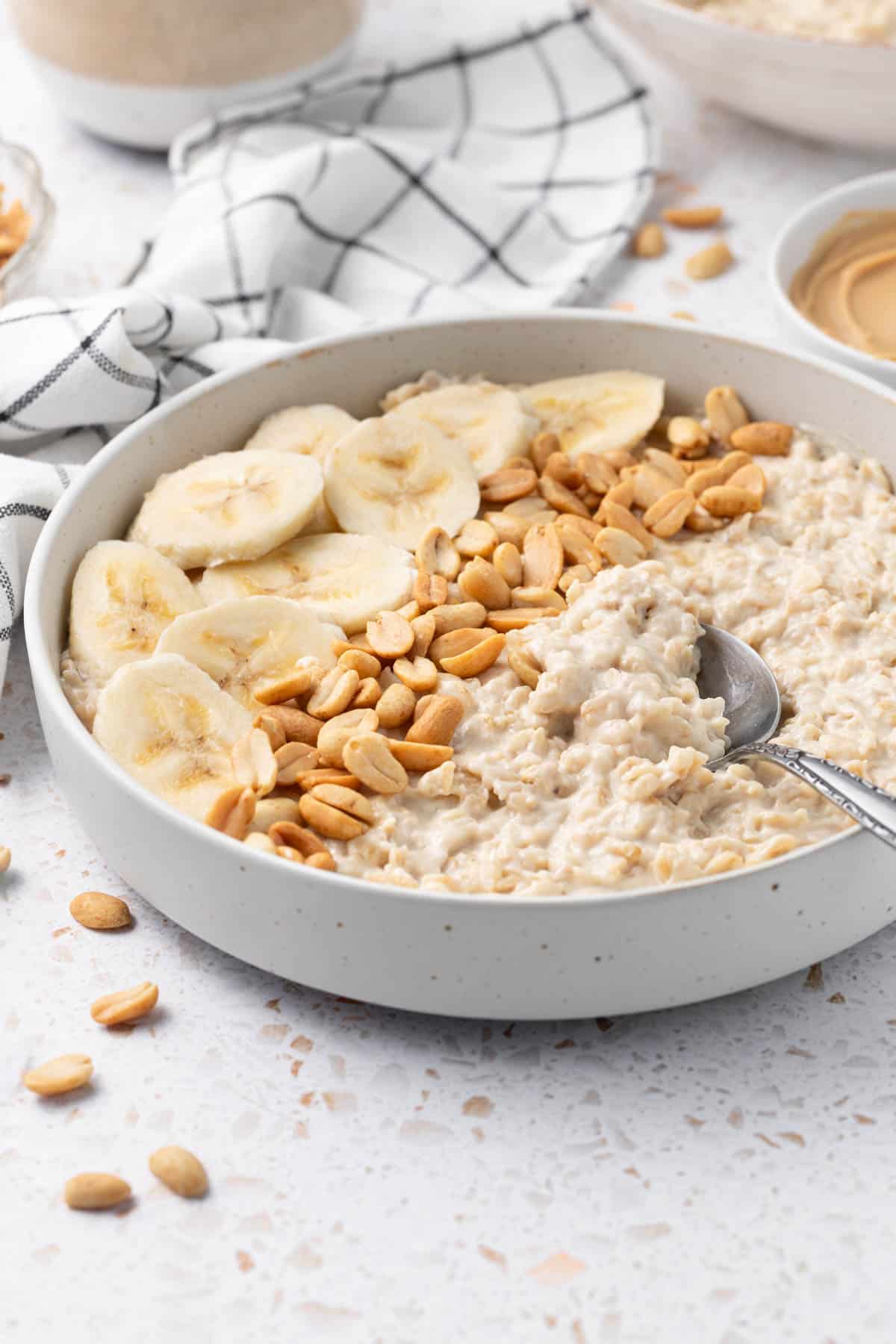 Bowl of Peanut Butter Porridge decorated with some banana slices and peanuts, with a spoon scooping some porridge.