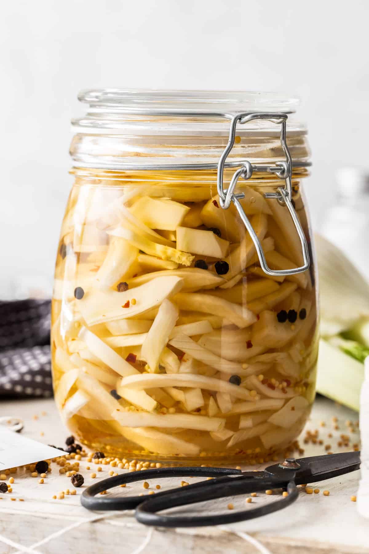 Jar of Pickled Fennel, sitting on a wooden board, with some herbs and spices around the edge.