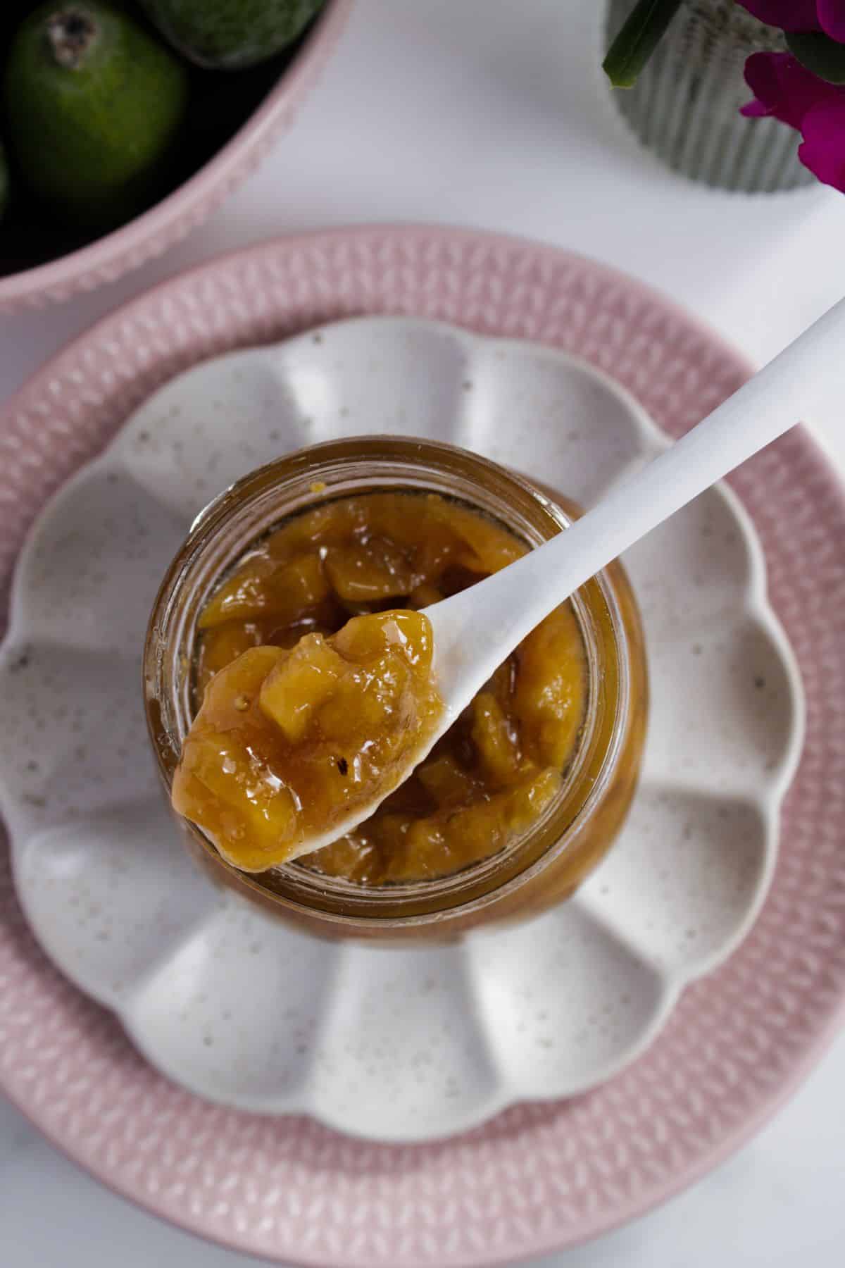 White spoon with some Feijoa Jam on it, sitting on top of open jar of jam.