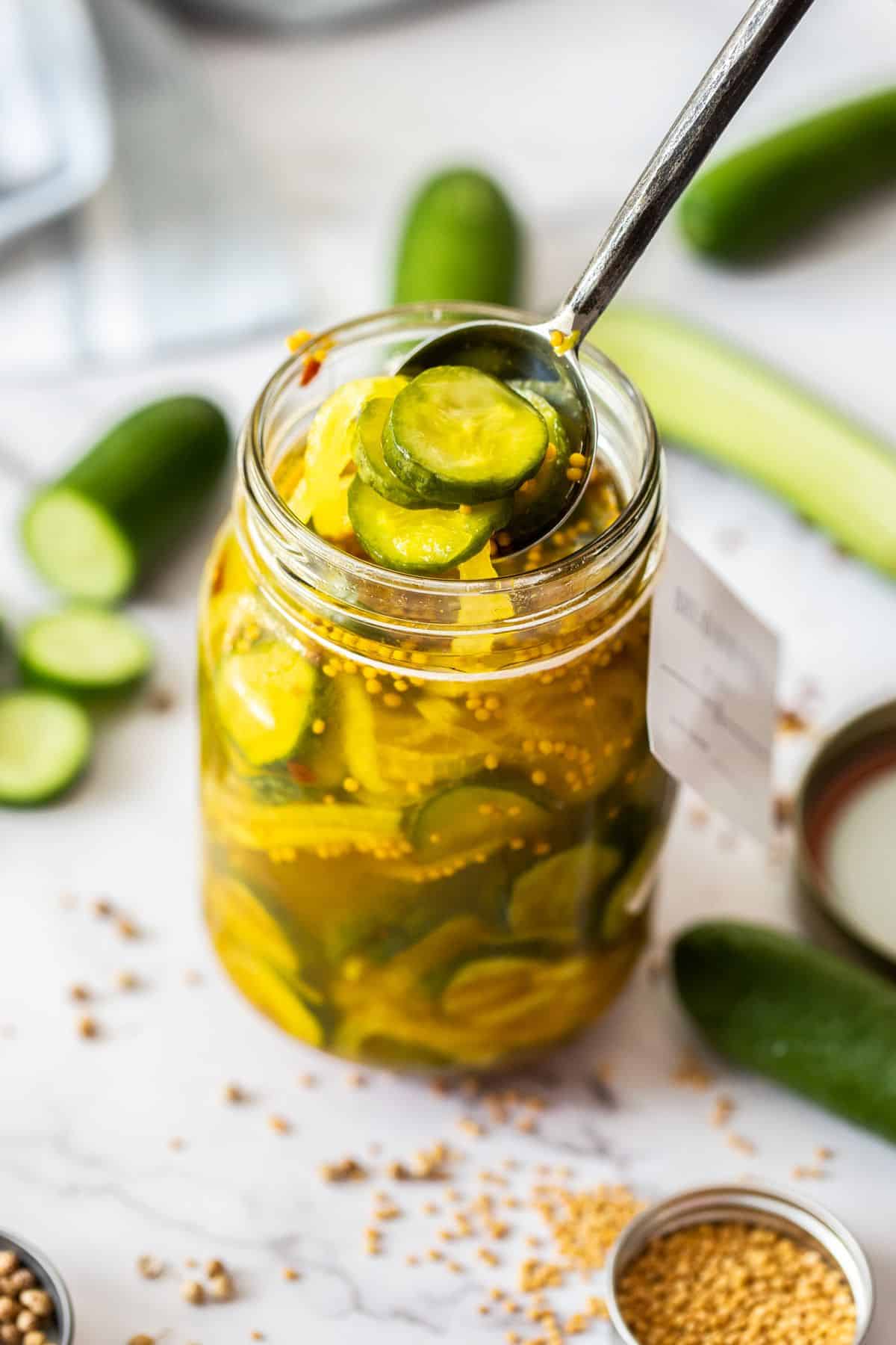 Jar of Bread and Butter Pickles, with a spoon reaching in to lift some pickles out of the jar.